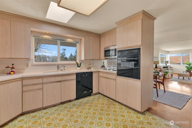 kitchen featuring a skylight, light brown cabinetry, sink, and black appliances