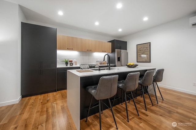 kitchen with a kitchen island with sink, high end fridge, a kitchen breakfast bar, light hardwood / wood-style floors, and light brown cabinets