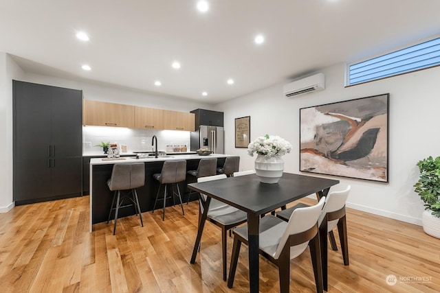 dining space with sink, light hardwood / wood-style floors, and an AC wall unit