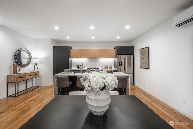 kitchen featuring high quality fridge, a wall mounted air conditioner, light brown cabinetry, a kitchen bar, and light wood-type flooring