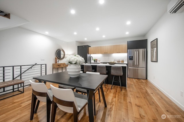 dining area featuring sink, a wall unit AC, and light wood-type flooring