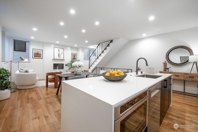 kitchen featuring sink, light hardwood / wood-style flooring, a kitchen island with sink, stainless steel microwave, and a fireplace