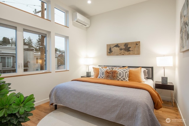 bedroom featuring a towering ceiling, light hardwood / wood-style flooring, and a wall unit AC