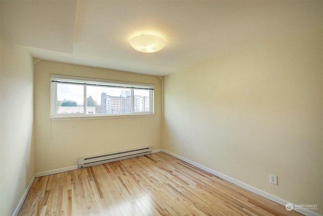 empty room featuring a baseboard heating unit and light hardwood / wood-style floors