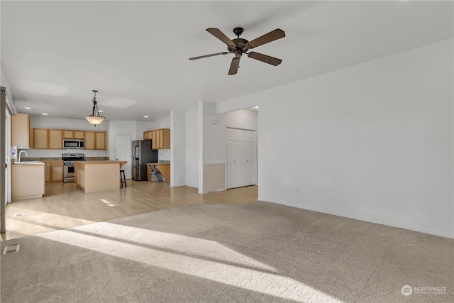 unfurnished living room featuring sink, light colored carpet, and ceiling fan