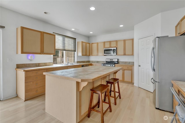 kitchen with appliances with stainless steel finishes, a kitchen bar, a kitchen island, and light hardwood / wood-style flooring