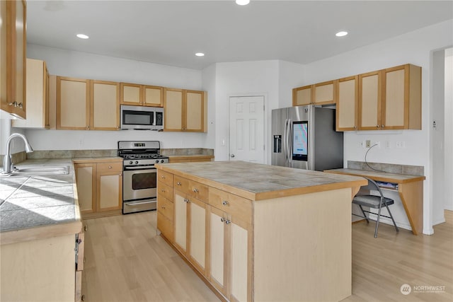 kitchen with appliances with stainless steel finishes, light brown cabinetry, sink, a center island, and light wood-type flooring