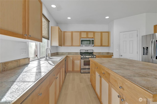 kitchen with sink, stainless steel appliances, a kitchen island, light brown cabinetry, and light wood-type flooring