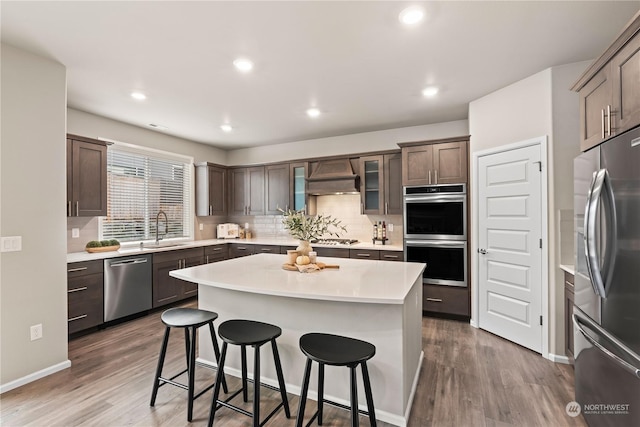 kitchen with premium range hood, sink, wood-type flooring, a kitchen island, and stainless steel appliances