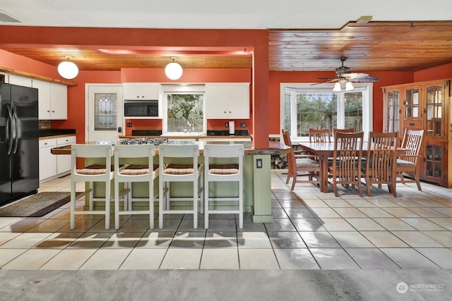 kitchen with wood ceiling, white cabinetry, a kitchen breakfast bar, light tile patterned flooring, and black refrigerator with ice dispenser