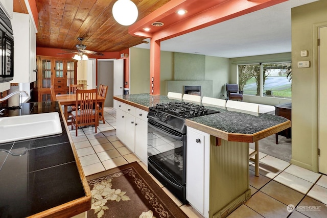 kitchen featuring white cabinetry, sink, a kitchen breakfast bar, light tile patterned floors, and black appliances