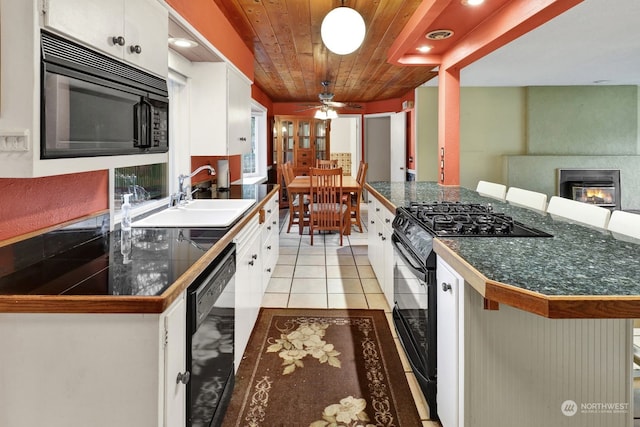 kitchen with sink, black appliances, a large fireplace, white cabinets, and a kitchen bar