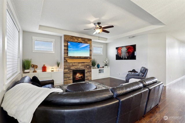 living room with a healthy amount of sunlight, dark hardwood / wood-style floors, a raised ceiling, and a stone fireplace