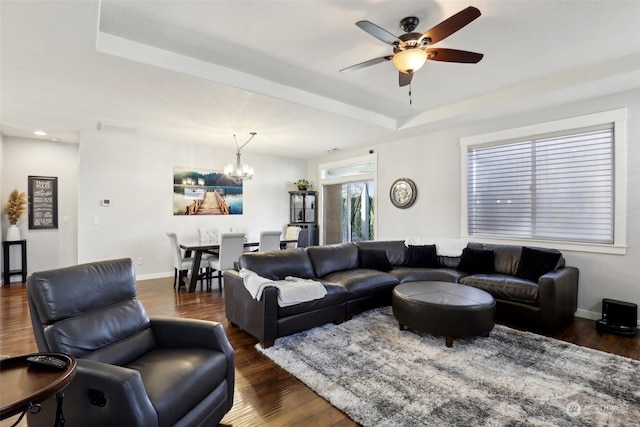 living room featuring dark hardwood / wood-style floors, a raised ceiling, and ceiling fan with notable chandelier