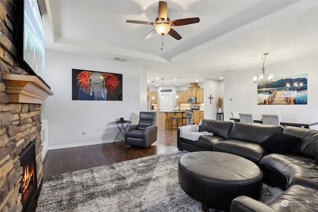 living room with sink, a tray ceiling, a fireplace, dark hardwood / wood-style flooring, and ceiling fan with notable chandelier