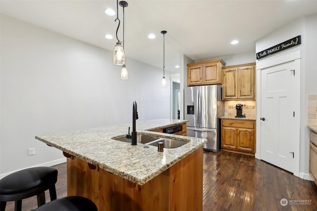 kitchen featuring sink, light stone counters, stainless steel fridge with ice dispenser, an island with sink, and pendant lighting