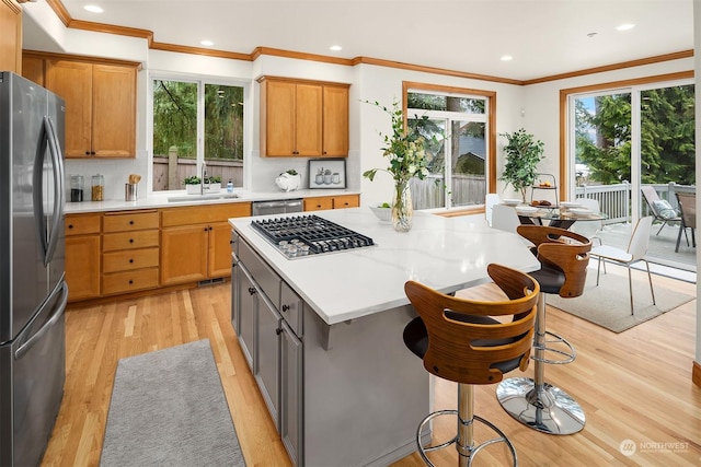 kitchen with appliances with stainless steel finishes, a kitchen breakfast bar, a center island, ornamental molding, and light wood-type flooring