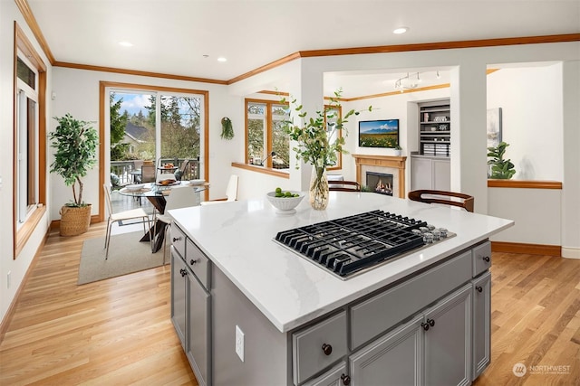 kitchen featuring stainless steel gas stovetop, gray cabinetry, ornamental molding, a center island, and light hardwood / wood-style flooring