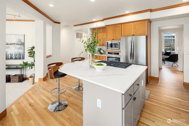 kitchen with crown molding, appliances with stainless steel finishes, gray cabinetry, a center island, and light wood-type flooring