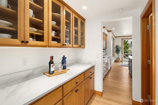 bar with light stone counters, crown molding, and light hardwood / wood-style flooring