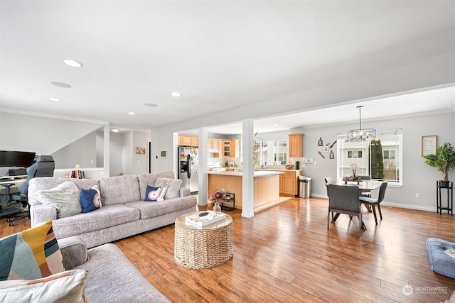 living room with crown molding, a chandelier, and light wood-type flooring