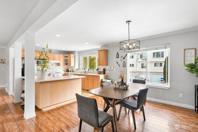 dining room featuring a notable chandelier, ornamental molding, sink, and light wood-type flooring