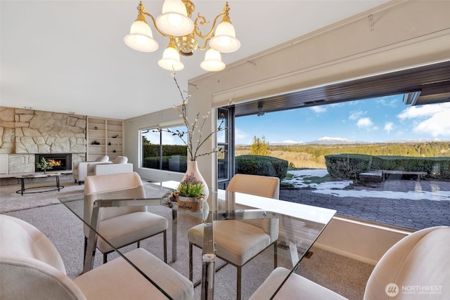 dining room with a stone fireplace, built in features, a chandelier, and carpet flooring