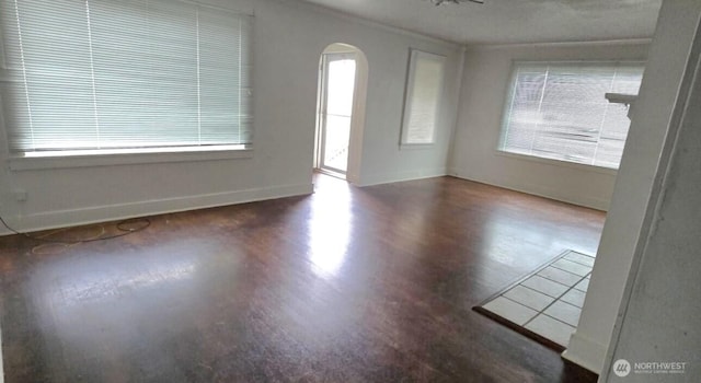 unfurnished room featuring arched walkways, baseboards, and wood finished floors