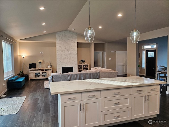 kitchen with white cabinetry, decorative light fixtures, light stone countertops, and lofted ceiling