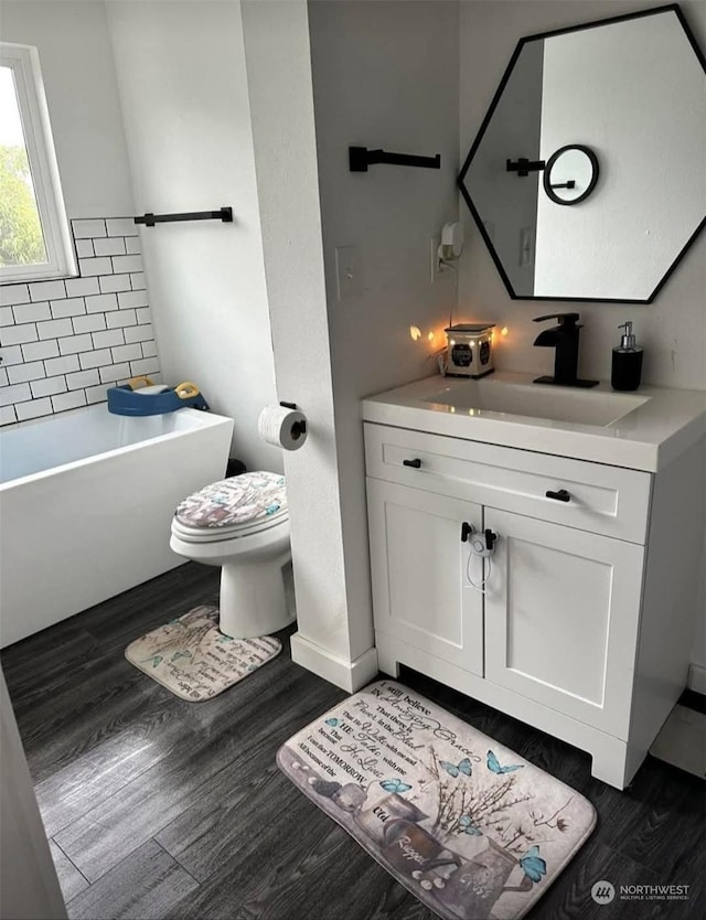 bathroom featuring wood-type flooring, a bath, vanity, and toilet