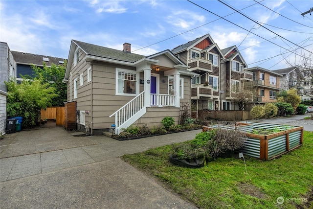 view of front of house featuring fence, a residential view, roof with shingles, a vegetable garden, and a chimney