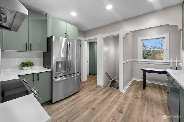 kitchen with tasteful backsplash, ventilation hood, light countertops, stainless steel fridge, and green cabinetry