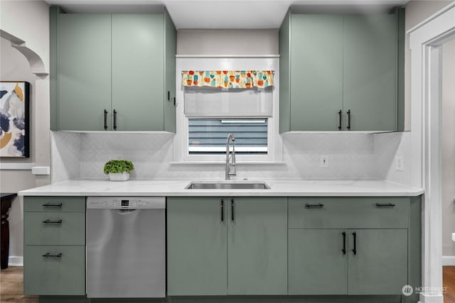 kitchen with green cabinets, decorative backsplash, stainless steel dishwasher, wood finished floors, and a sink