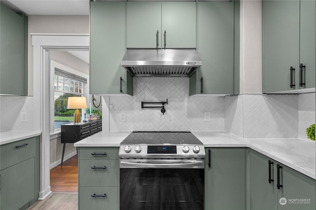 kitchen with light wood finished floors, tasteful backsplash, green cabinets, extractor fan, and electric range