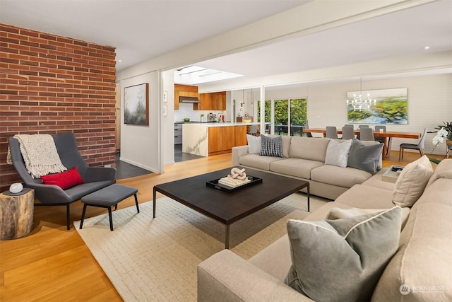 living room with brick wall, a chandelier, and light hardwood / wood-style flooring