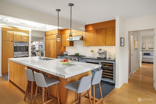 kitchen with wine cooler, sink, a center island with sink, pendant lighting, and light hardwood / wood-style floors