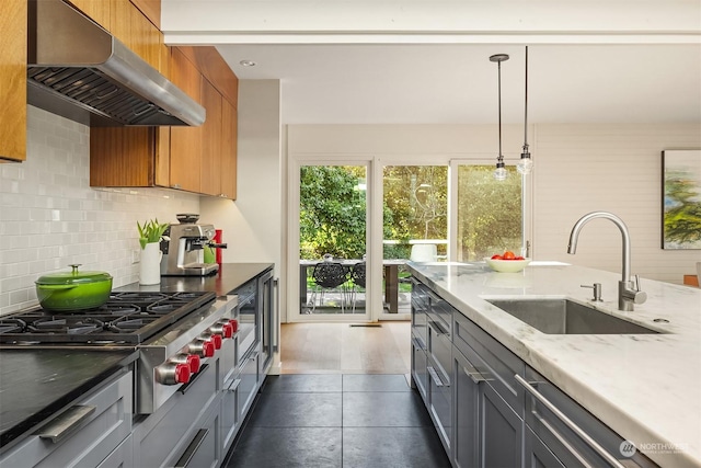 kitchen with stainless steel gas stovetop, sink, hanging light fixtures, exhaust hood, and light stone countertops