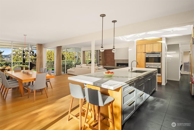 kitchen featuring pendant lighting, a fireplace, sink, light stone counters, and a center island with sink