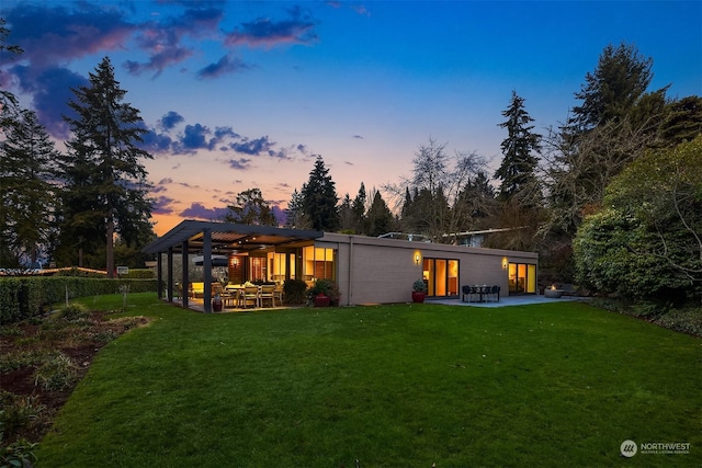 back house at dusk featuring a patio, a yard, and a pergola