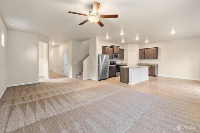 kitchen with appliances with stainless steel finishes, sink, dark brown cabinetry, light carpet, and a center island with sink