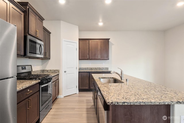 kitchen featuring sink, a kitchen island with sink, dark brown cabinetry, stainless steel appliances, and light wood-type flooring