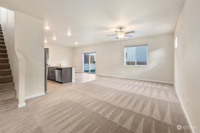 unfurnished living room featuring ceiling fan, sink, and light carpet