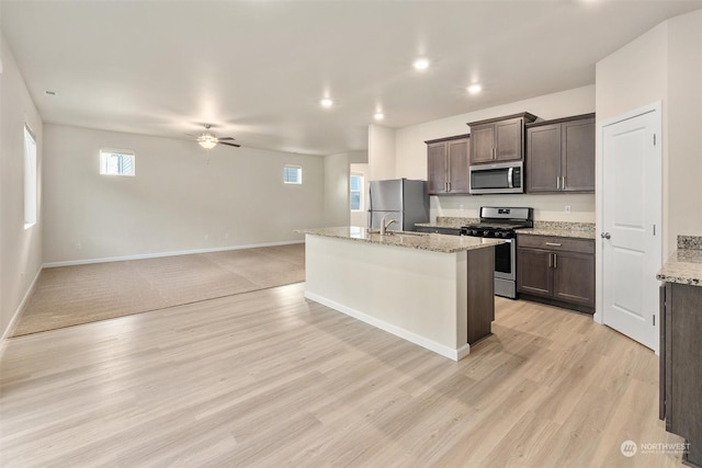 kitchen featuring sink, light hardwood / wood-style flooring, appliances with stainless steel finishes, light stone countertops, and a kitchen island with sink