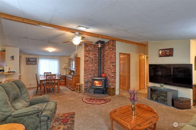 living room featuring vaulted ceiling with beams, ceiling fan, carpet flooring, and a wood stove