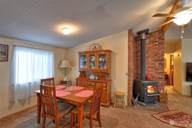 carpeted dining area with vaulted ceiling, a wood stove, a textured ceiling, and ceiling fan