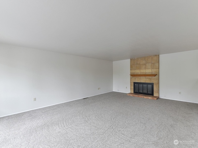 unfurnished living room featuring a tiled fireplace and carpet flooring