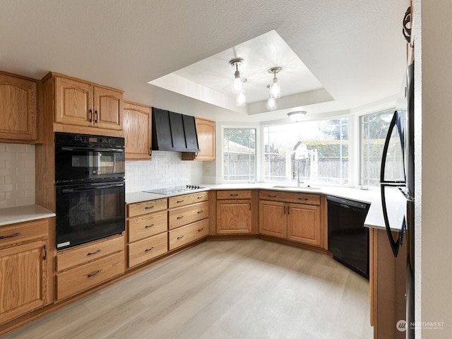 kitchen featuring wall chimney exhaust hood, sink, light hardwood / wood-style flooring, a tray ceiling, and black appliances