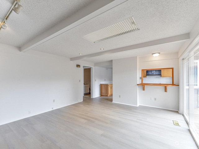 unfurnished living room featuring beam ceiling, light hardwood / wood-style floors, and a textured ceiling