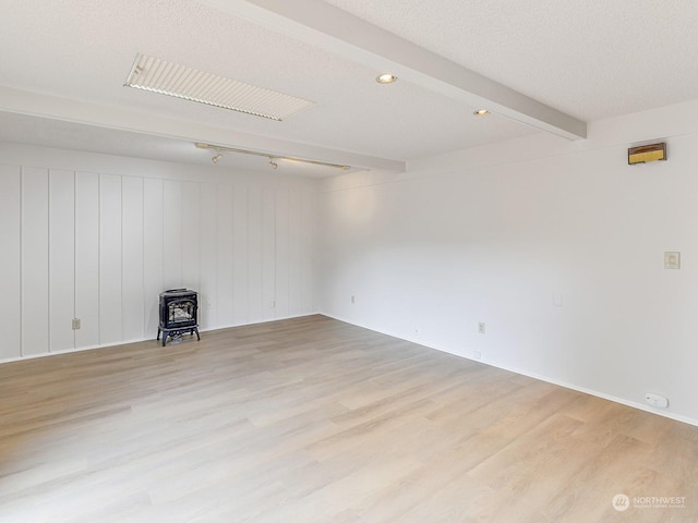 spare room featuring a textured ceiling, light wood-type flooring, beamed ceiling, and a wood stove