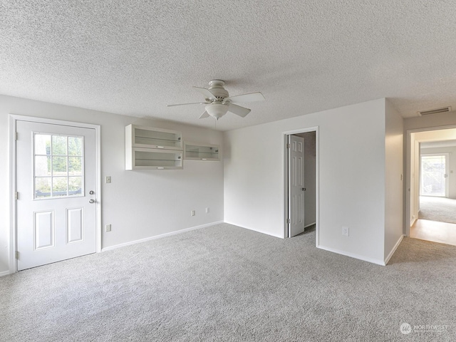 unfurnished living room featuring ceiling fan, carpet flooring, a textured ceiling, and a wealth of natural light